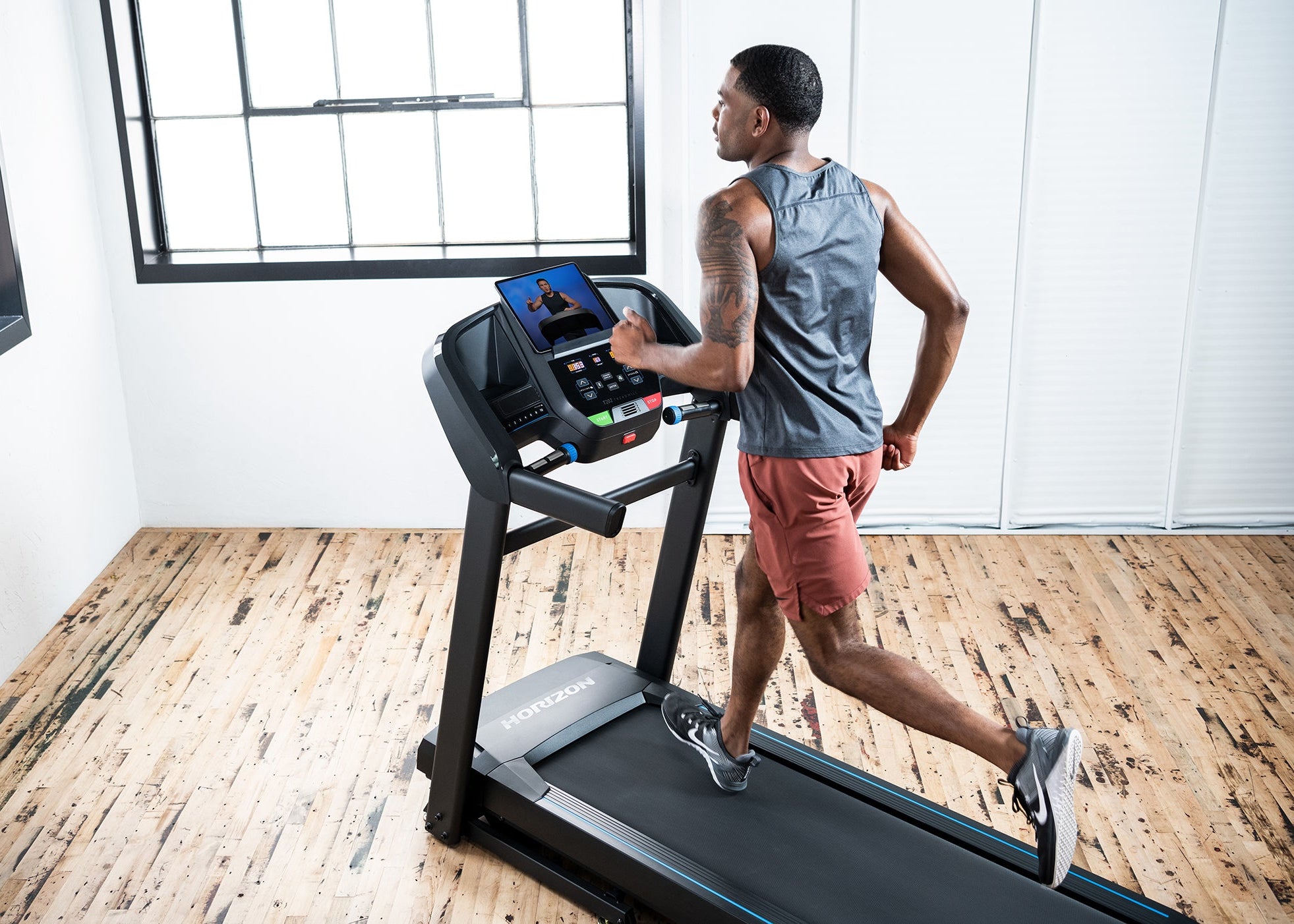 A man running on the Horizon T202 in a bright room with a wooden floor