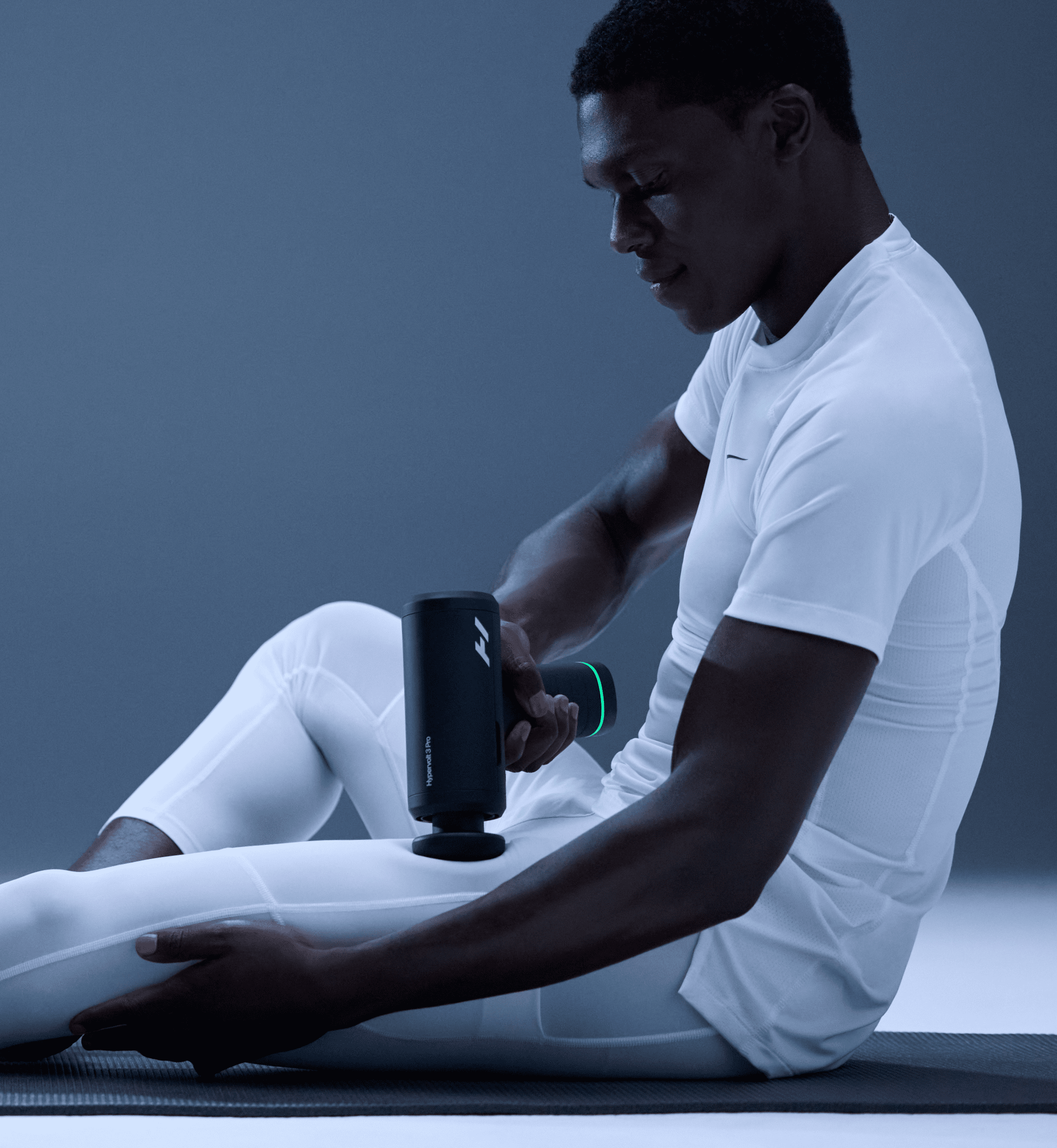 Hypervolt 3 Pro in use, a man seated on a mat treating his leg with the gun